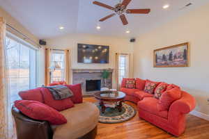 Living room featuring wood finished floors, lofted ceiling, recessed lighting, ceiling fan, and a stone fireplace