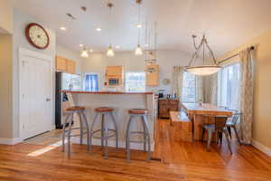 Kitchen with a kitchen bar, light wood finish cabinetry, lofted ceiling, stainless steel appliances, and light wood-style flooring