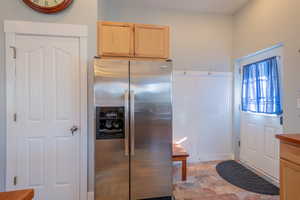 Kitchen with stainless steel fridge with ice dispenser, stone finish floors, and light wood finish cabinets