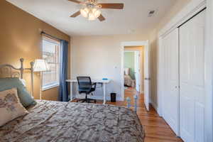 Bedroom featuring light wood-style flooring, a desk, a ceiling fan, and a closet