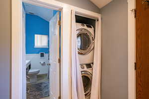 Laundry area featuring vaulted ceiling, stacked washer and clothes dryer, a wainscoted wall, and light tile patterned floors