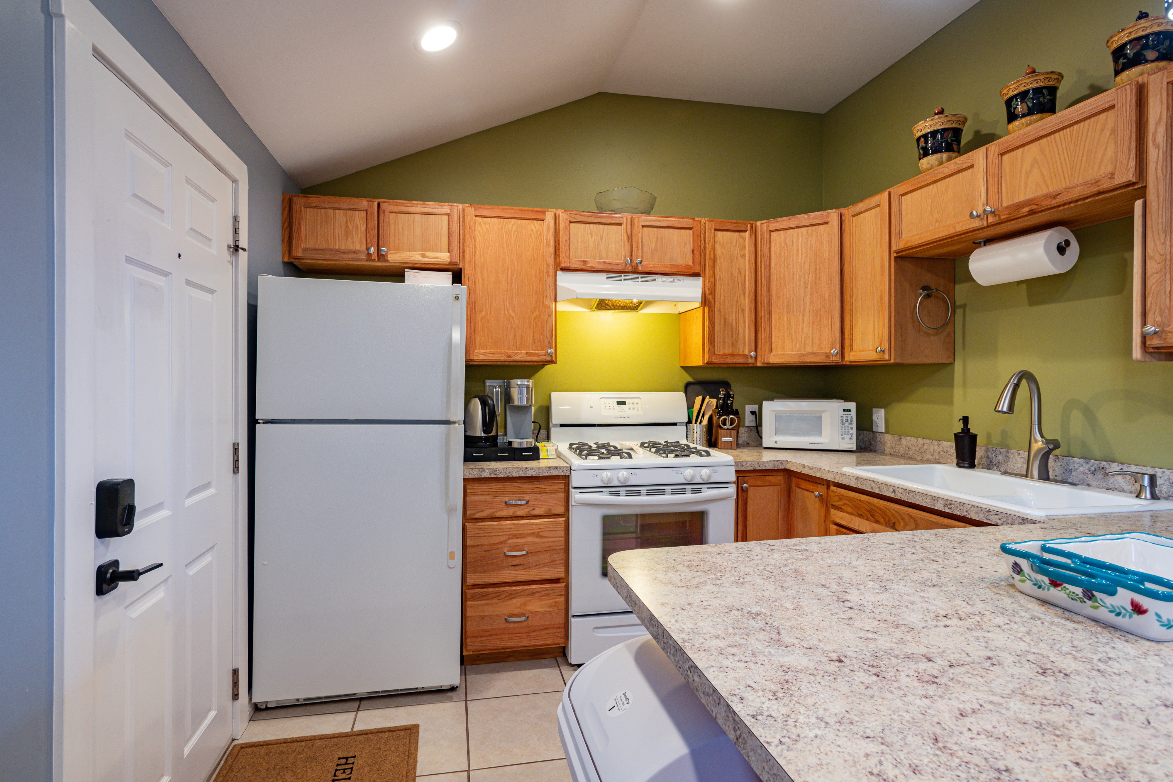 Kitchen with white appliances, light countertops, lofted ceiling, light tile patterned floors, and a peninsula