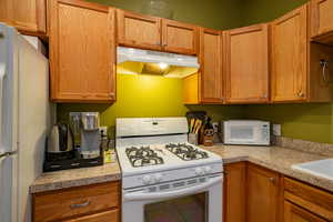 Kitchen with white appliances, light countertops, and wood finish cabinetry