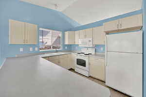 Kitchen with white appliances, light countertops, vaulted ceiling, and light tile patterned floors