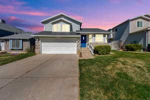 View of front of property featuring a yard, a garage, concrete driveway, stone siding, and roof with shingles