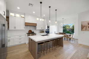 Dual tone kitchen featuring light stone countertops, a center island with sink, light wood-style flooring, a kitchen breakfast bar, and dual tone cabinetry