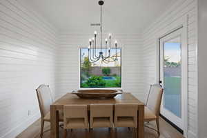 Dining space with wood finished floors, hanging lights, wooden walls, and crown molding