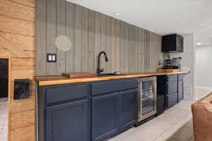 Indoor wet bar with wood counters, wooden walls, beverage cooler, light tile patterned flooring, and recessed lighting