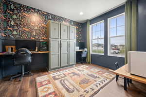 Office area with wallpapered walls, dark wood-type flooring, and built in desk