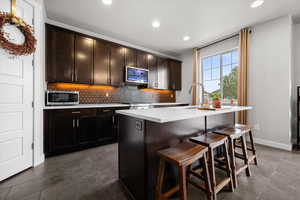 Kitchen with dark wood finish cabinetry, a kitchen island with sink, a breakfast bar area, stainless steel appliances, and tasteful backsplash