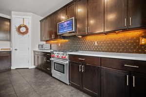 Kitchen featuring dark wood finish cabinetry, stainless steel appliances, decorative backsplash, dark tile patterned floors, and light stone counters