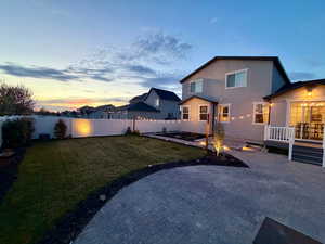 Back of property at dusk featuring stucco siding, a patio, a fenced backyard, and a residential view