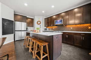 Kitchen with dark wood finish cabinetry, stainless steel appliances, a center island with sink, a breakfast bar, and recessed lighting