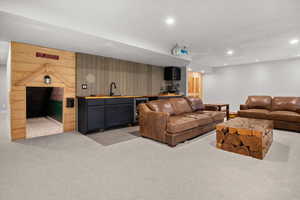 Living room with light carpet, beverage cooler, wet bar, wood walls, and recessed lighting