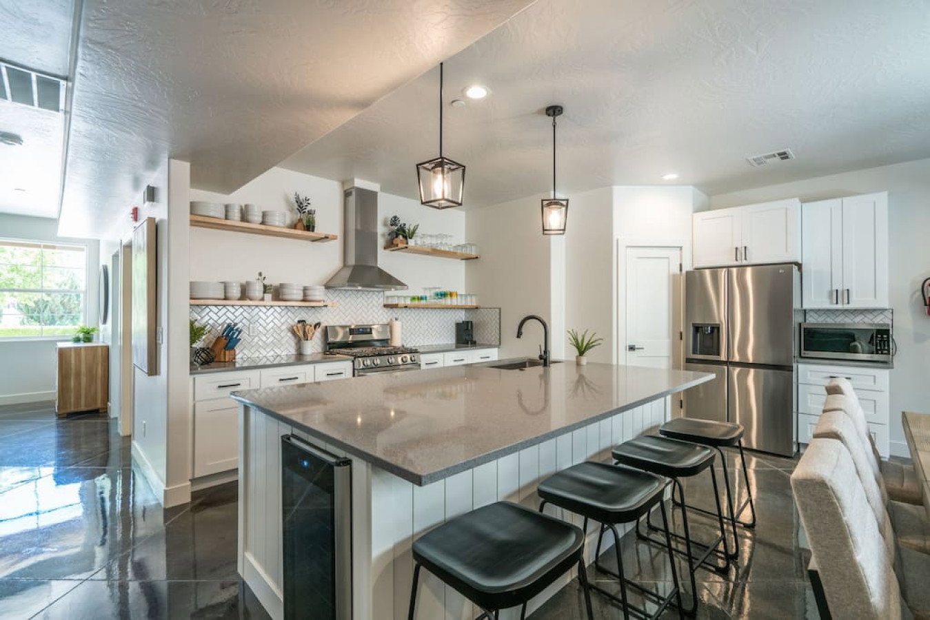 Kitchen with white cabinetry, stainless steel appliances, dark stone countertops, a kitchen bar, and a kitchen island with sink