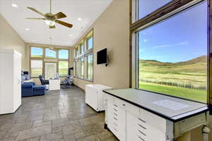 Kitchen featuring stone tile floors, a ceiling fan, white cabinetry, a high ceiling, and pendant lighting