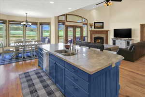 Kitchen with blue cabinets, open floor plan, light wood finished floors, a lit fireplace, and an island with sink
