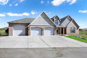 View of front facade featuring a garage, brick siding, driveway, and board and batten siding