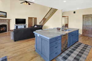 Kitchen featuring open floor plan, an island with sink, light wood-style flooring, a fireplace, and stainless steel dishwasher