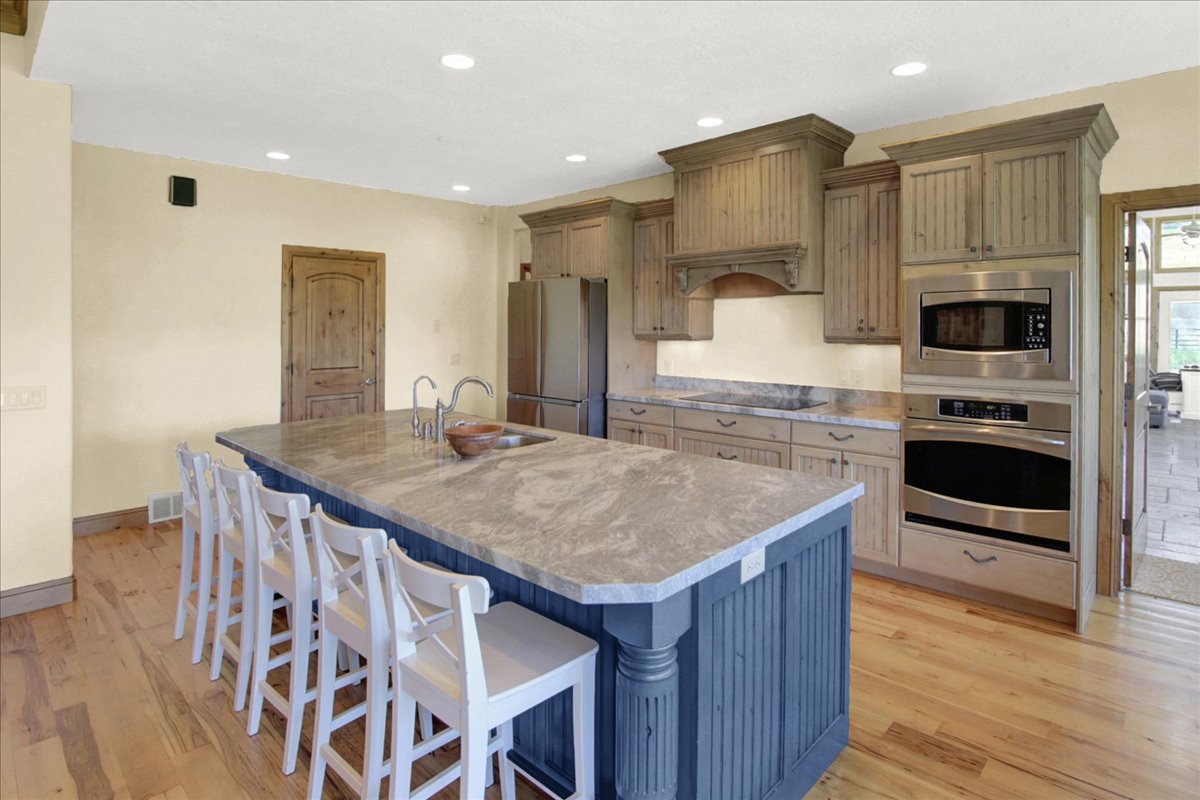 Kitchen with stainless steel appliances, a breakfast bar, a large island with sink, light wood-style floors, and recessed lighting