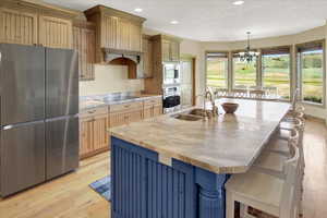 Two tone kitchen with light wood finished floors, stainless steel appliances, a kitchen breakfast bar, a large island with sink, and a chandelier