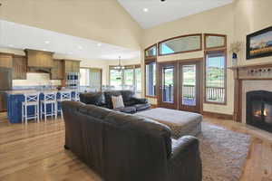 Living room with light wood-style flooring, a tiled fireplace, lofted ceiling, and suspended lighting