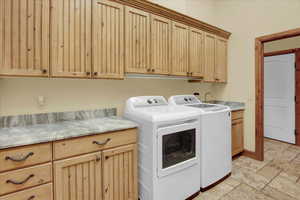 Laundry area featuring stone tile floors, cabinet space, and washer and dryer
