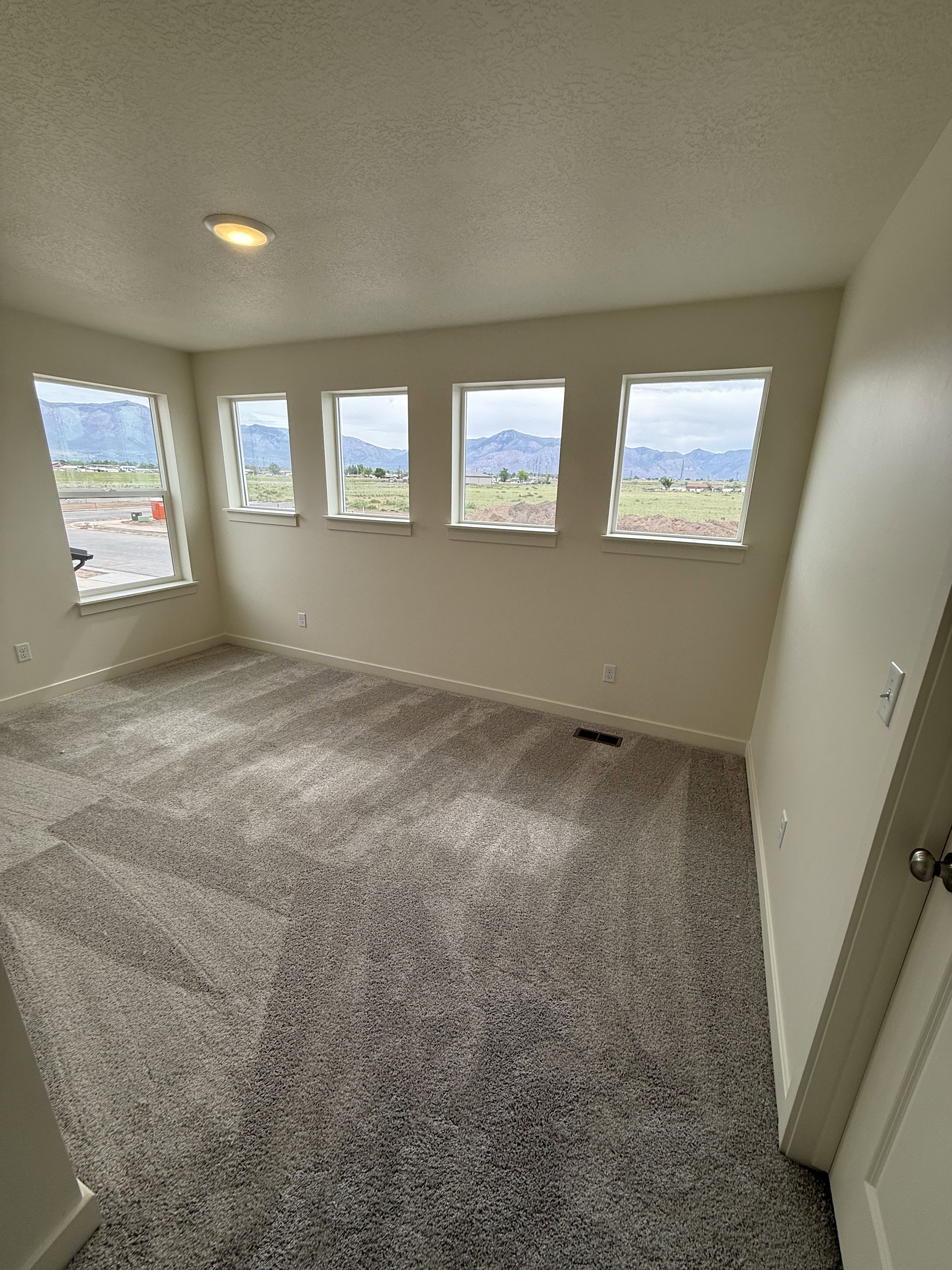 Spacious room featuring multiple windows, neutral wall paint, and plush gray carpeting