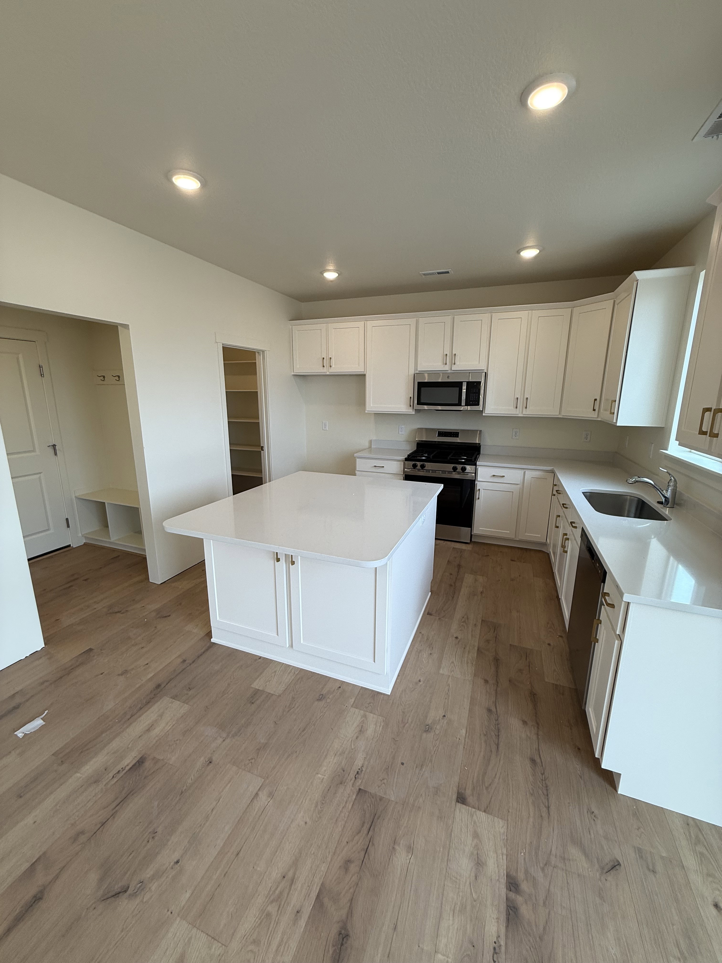 Kitchen featuring wood-finish flooring, recessed lighting, white cabinetry, a central island with a solid surface countertop, and stainless steel appliances