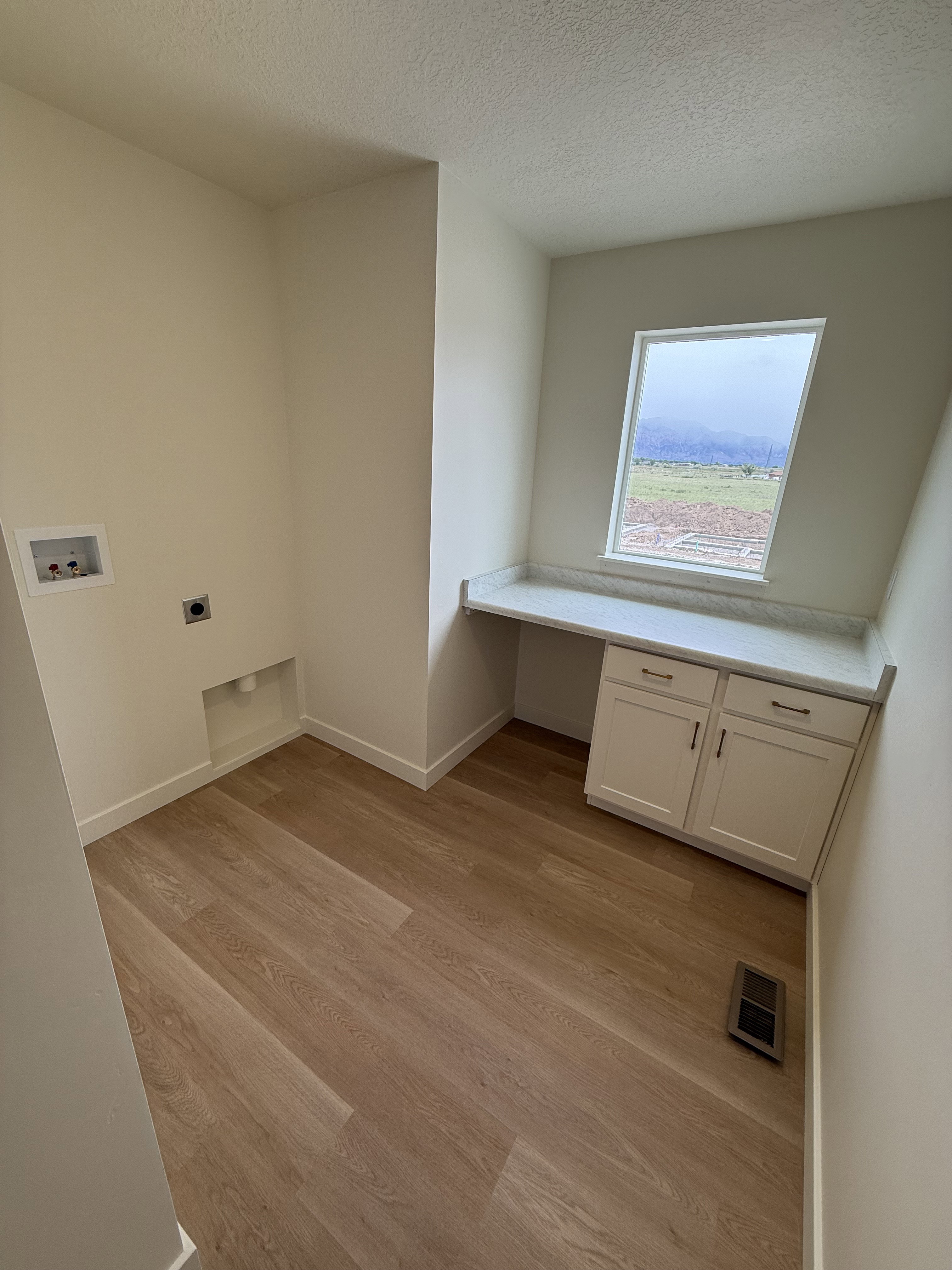 Laundry area featuring wood-finish flooring, light-toned walls, a built-in countertop with lower cabinetry, and a window providing natural light