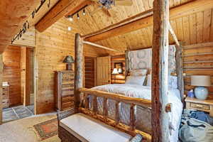 Bedroom featuring lofted ceiling with beams, rustic walls, rail lighting, ceiling fan, and wood ceiling
