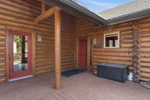 Doorway to property featuring log exterior, a deck, and roof with shingles