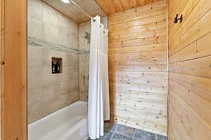 Full bathroom featuring shower / tub combo, dark stone finish flooring, wood walls, and recessed lighting