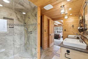 Ensuite bathroom featuring stone tile flooring, double vanity, a shower stall, recessed lighting, and wood ceiling