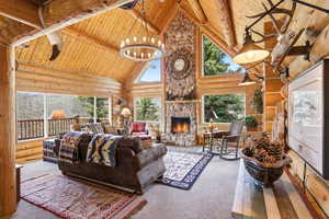 Carpeted living area with hanging lights, a high wood beamed ceiling, log walls, and a stone fireplace