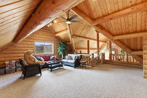 Living room with log walls, light colored carpet, a ceiling fan, vaulted ceiling with beams, and wooden ceiling