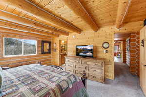 Bedroom featuring rustic walls, light colored carpet, a wooden ceiling with exposed beams, and wooden walls