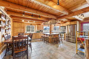 Dining space with track lighting, stone tile flooring, healthy amount of natural light, and a wooden ceiling with exposed beams