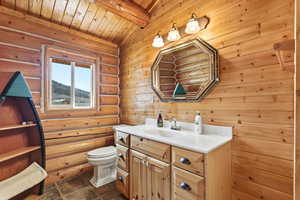 Half bathroom featuring vanity, log walls, and a wooden ceiling with exposed beams
