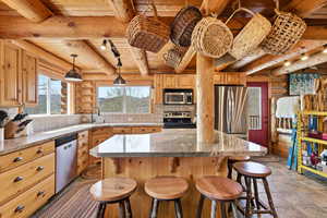 Kitchen featuring rustic walls, stainless steel appliances, light stone countertops, a kitchen breakfast bar, and pendant lighting