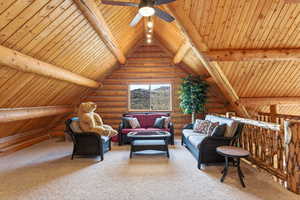 Sitting room with log walls, a wooden ceiling with exposed beams, carpet, and a ceiling fan