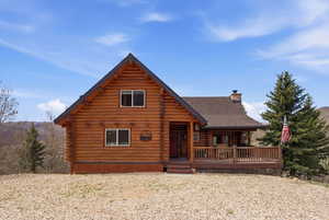 View of front facade featuring log siding, a chimney, covered porch, and roof with shingles