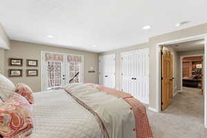Bedroom featuring multiple closets, access to outside, light carpet, french doors, and a textured ceiling