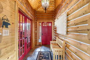 Foyer entrance featuring french doors, a vaulted wood ceiling, log walls, dark stone finish floors, and a chandelier