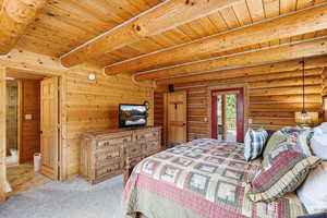 Carpeted bedroom featuring access to outside, wooden walls, rustic walls, and a wood ceiling with exposed beams