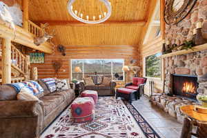 Living room with log walls, stone tile flooring, a fireplace, and a high wood beamed ceiling