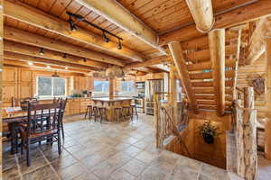 Dining room featuring track lighting, a wooden ceiling with exposed beams, stone tile flooring, and log walls