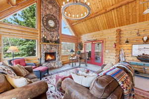 Living area with rustic walls, french doors, a stone fireplace, a chandelier, and a high wood beamed ceiling