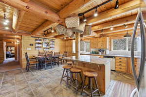 Kitchen featuring track lighting, stainless steel appliances, light countertops, a wood ceiling with exposed beams, and a kitchen bar