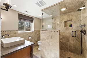 Full bathroom with vanity, a stall shower, a wainscoted wall, and tile walls